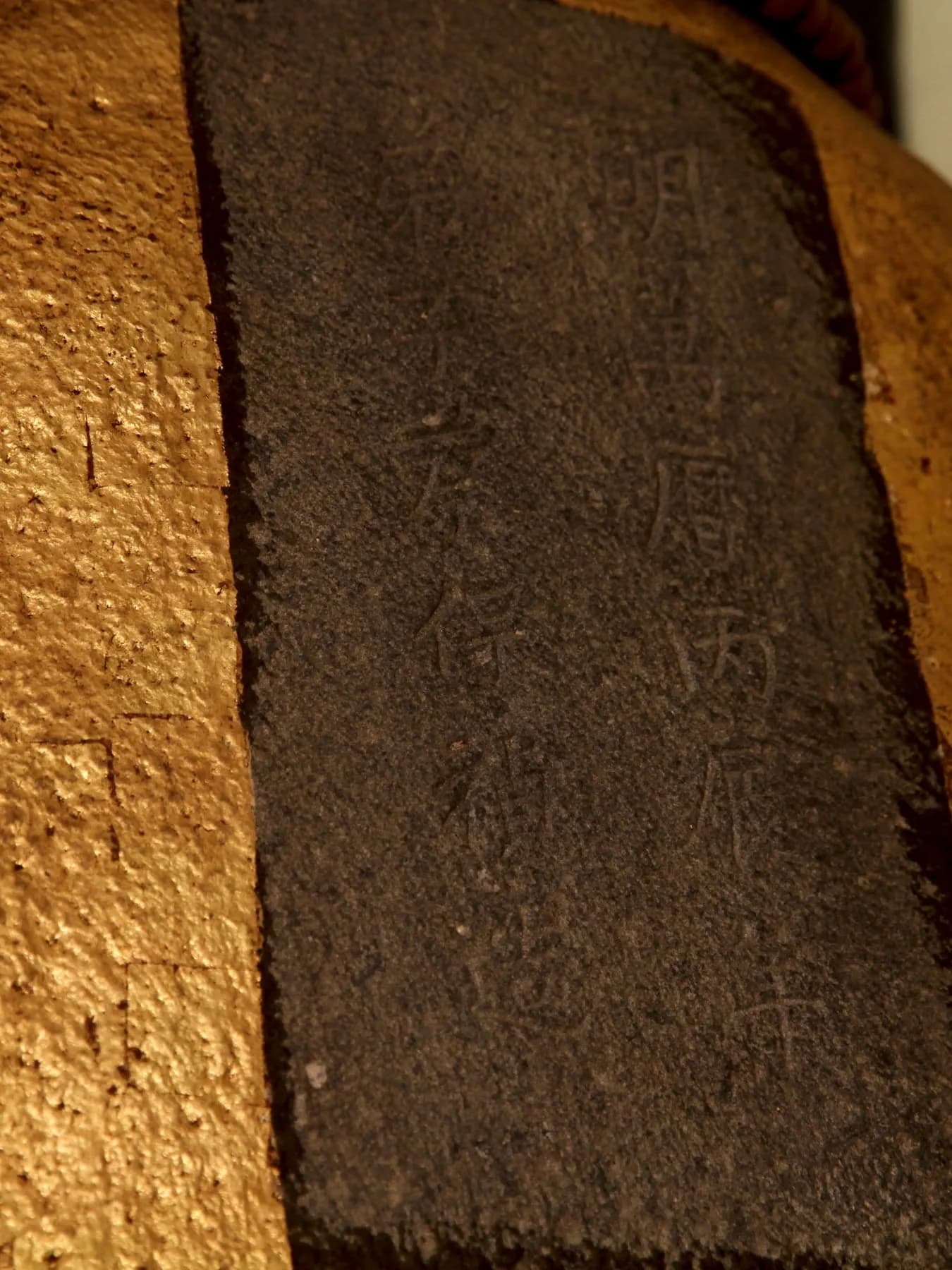鎮殿觀音佛祖石像背面刻款特寫：金色石像背上一塊深色刻面，兩行陰刻，右行「明萬曆丙辰年」，左行為造像弟子題名（攝於 2015 年）