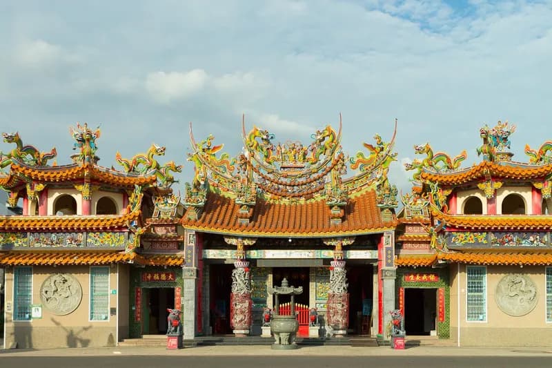 新化保生大帝廟正面全景：三川殿居中，左右各一座鐘鼓樓，屋頂剪黏襯著藍天，前為廟埕