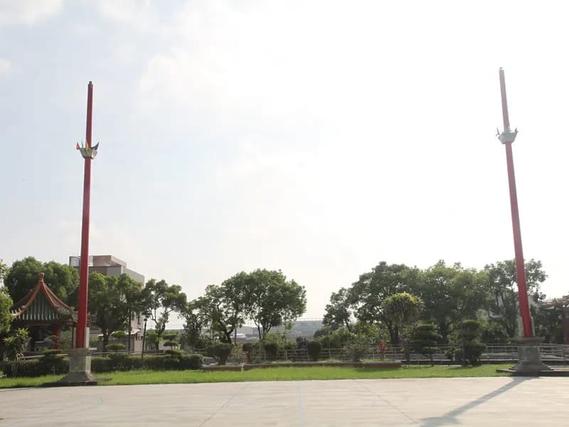 本廟廟埕:寬闊的廣場兩側各立一根紅色旗桿,旁邊有綠瓦涼亭與樹木(攝於 2015 年)